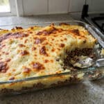 Escondidinho de carne moída com batata em travessa de vidro sobre a bancada da cozinha, com uma porção servida mostrando a camada de carne moída