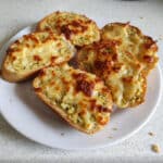 Pão de alho caseiro com queijo gratinado em prato branco na bancada da cozinha