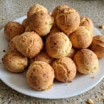 Prato com pães de queijo fit dourados e um pouco irregulares sobre a bancada da cozinha