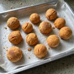 Assadeira com pãezinhos fit de batata-doce dourados com chia sobre papel-manteiga, na bancada da cozinha